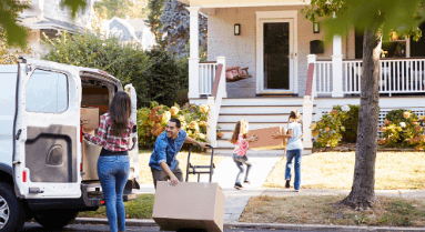 A family unloads moving boxes from a van and carries them toward their new house on a sunny day, symbolizing moving into a new home and fresh beginnings.